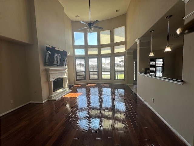 unfurnished living room with a fireplace with raised hearth, a high ceiling, wood finished floors, a ceiling fan, and baseboards