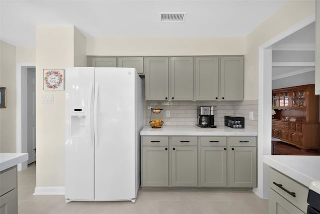 kitchen with decorative backsplash, crown molding, white refrigerator with ice dispenser, light tile patterned floors, and gray cabinets