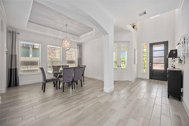 dining area with arched walkways, a tray ceiling, visible vents, light wood-style flooring, and baseboards