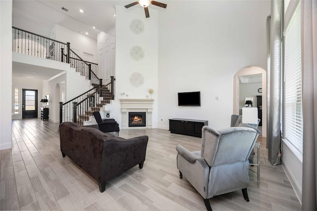 living area with arched walkways, visible vents, light wood-style floors, a warm lit fireplace, and stairs