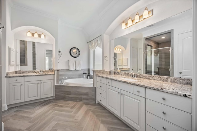 bathroom featuring a garden tub, two vanities, a sink, a stall shower, and crown molding