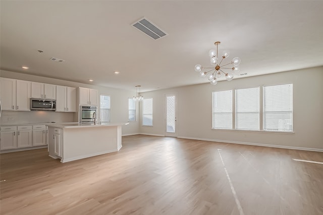 kitchen with stainless steel appliances, pendant lighting, white cabinets, a notable chandelier, and a center island with sink