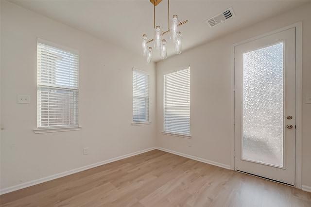 unfurnished dining area with light hardwood / wood-style floors, an inviting chandelier, and a wealth of natural light