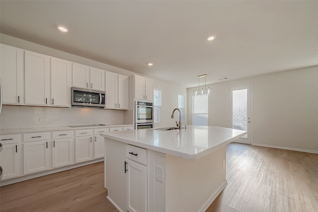 kitchen with light hardwood / wood-style flooring, appliances with stainless steel finishes, sink, and an island with sink