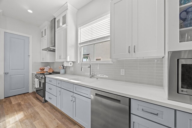 26831 Bay Water Dr, Galveston, TX 77554 - kitchen featuring wall chimney range hood, a sink, light wood-style floors, stainless steel appliances, and backsplash