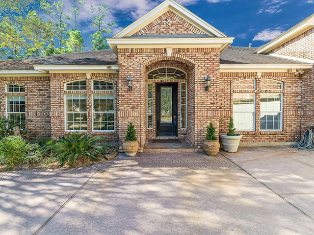 view of exterior entry with brick siding and roof with shingles