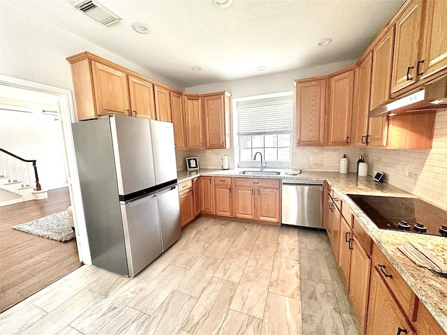 kitchen featuring light stone countertops, stainless steel appliances, sink, backsplash, and light wood-type flooring