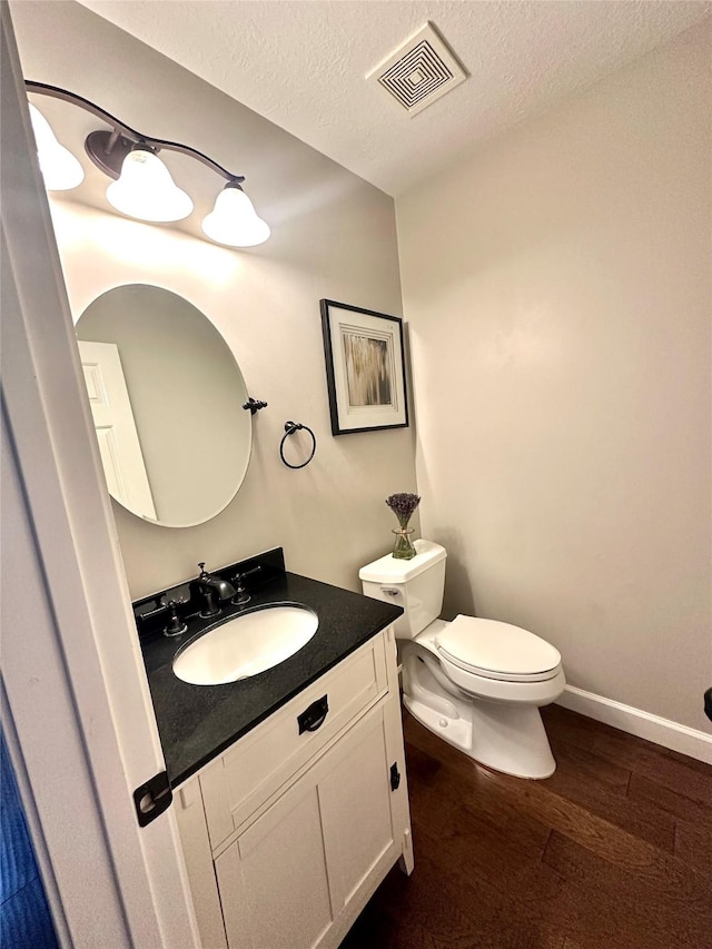 bathroom with wood-type flooring, a textured ceiling, toilet, and vanity