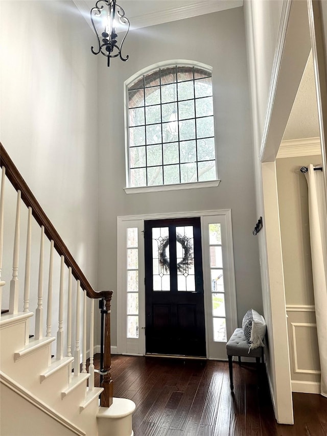 foyer entrance with a high ceiling, dark hardwood / wood-style flooring, crown molding, and a notable chandelier