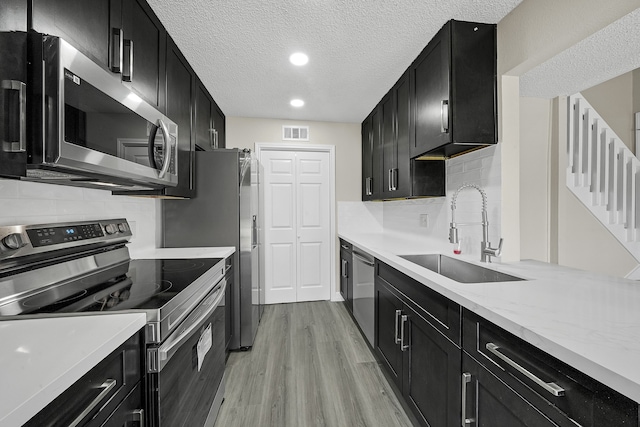 kitchen with appliances with stainless steel finishes, sink, a textured ceiling, decorative backsplash, and light hardwood / wood-style flooring