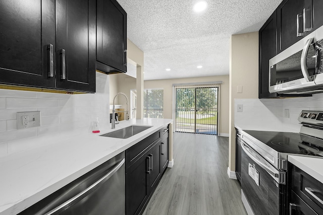 kitchen featuring stainless steel appliances, backsplash, sink, light wood-type flooring, and a textured ceiling