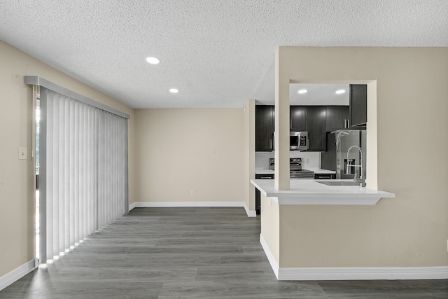 interior space featuring dark wood-type flooring, appliances with stainless steel finishes, a textured ceiling, and kitchen peninsula