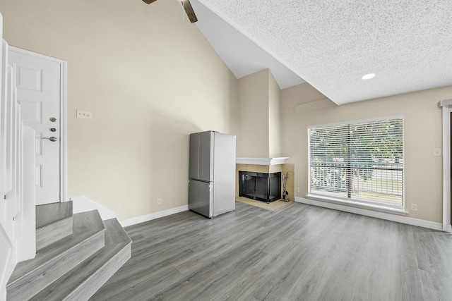 unfurnished living room featuring light hardwood / wood-style floors, a textured ceiling, lofted ceiling, and a multi sided fireplace