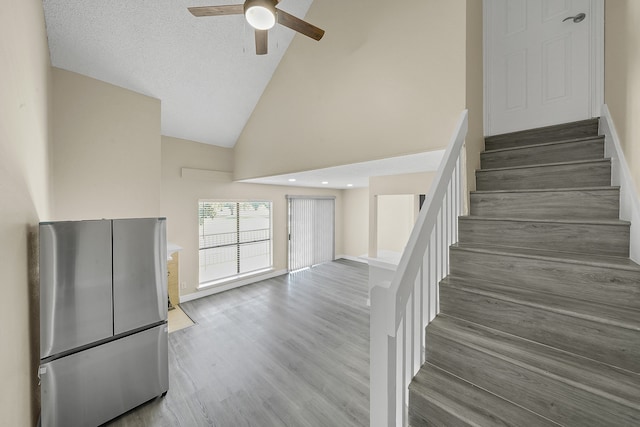 stairway with ceiling fan, high vaulted ceiling, a textured ceiling, and wood-type flooring