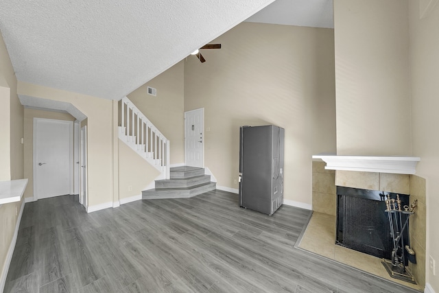 unfurnished living room featuring a textured ceiling, a tiled fireplace, high vaulted ceiling, and wood-type flooring