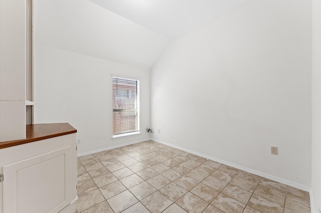 tiled empty room featuring lofted ceiling