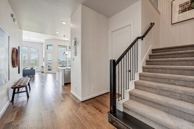 stairway featuring wood-type flooring, a textured ceiling, and a chandelier