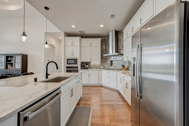 kitchen with wall chimney exhaust hood, sink, appliances with stainless steel finishes, and white cabinetry