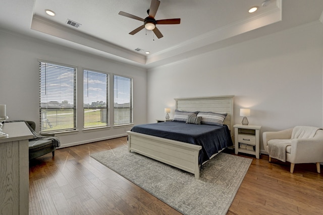 bedroom with ceiling fan, a raised ceiling, ornamental molding, and hardwood / wood-style floors