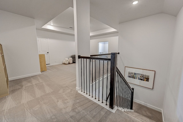 hall with a raised ceiling and light colored carpet