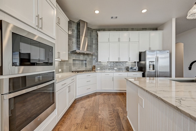 kitchen with wall chimney range hood, white cabinets, light hardwood / wood-style flooring, sink, and stainless steel appliances