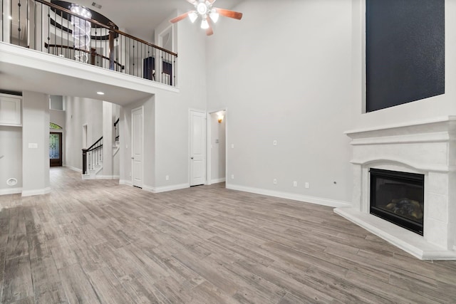 unfurnished living room featuring ceiling fan, plenty of natural light, a towering ceiling, and hardwood / wood-style flooring