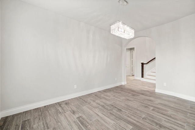 spare room with a notable chandelier and light wood-type flooring