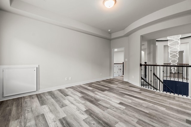 empty room with a raised ceiling, light hardwood / wood-style flooring, and a chandelier