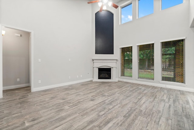 unfurnished living room with a towering ceiling, light hardwood / wood-style flooring, and ceiling fan