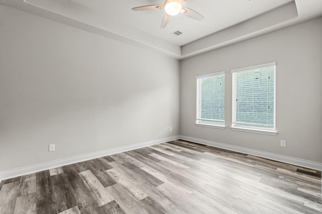 empty room featuring a tray ceiling, ceiling fan, and light wood-type flooring