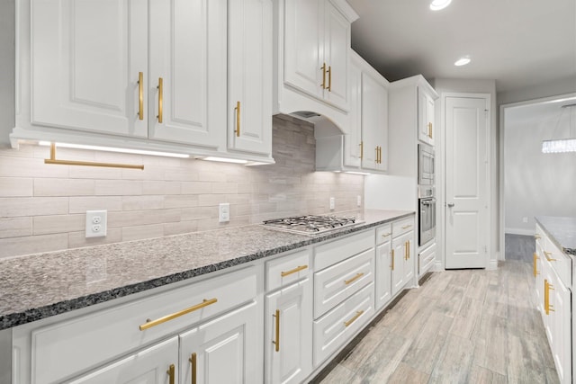 kitchen with stainless steel appliances, dark stone counters, light hardwood / wood-style floors, decorative backsplash, and white cabinets