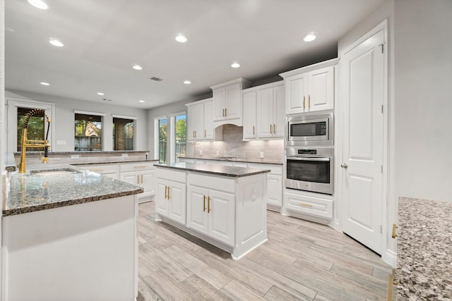 kitchen with kitchen peninsula, appliances with stainless steel finishes, dark stone countertops, a center island, and white cabinetry