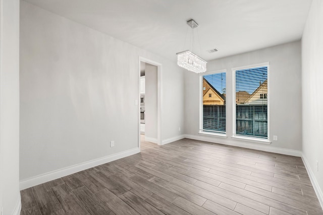 spare room with a chandelier and wood-type flooring