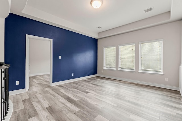 unfurnished room with a raised ceiling and light hardwood / wood-style flooring