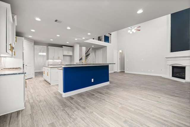 kitchen with white cabinets, ceiling fan, light hardwood / wood-style flooring, and an island with sink