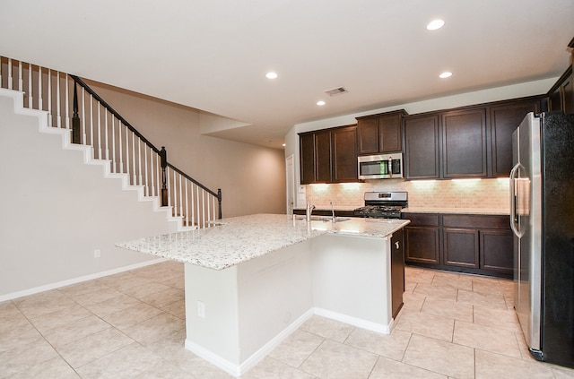 kitchen featuring backsplash, a kitchen island with sink, light stone countertops, sink, and stainless steel appliances