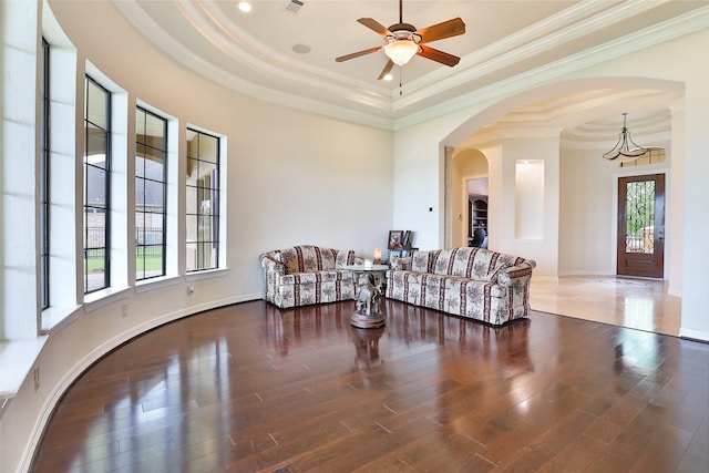 living room with a raised ceiling, ceiling fan, dark wood-type flooring, and ornamental molding