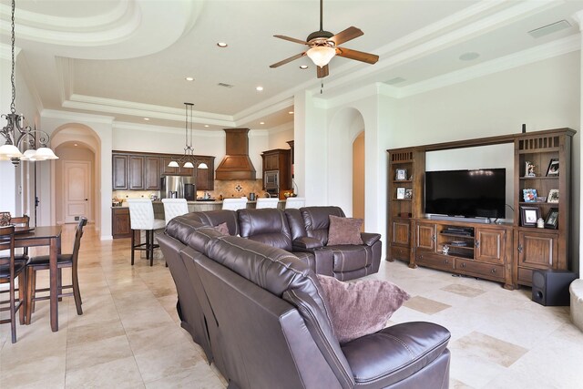 tiled living room featuring ceiling fan with notable chandelier, crown molding, and a tray ceiling