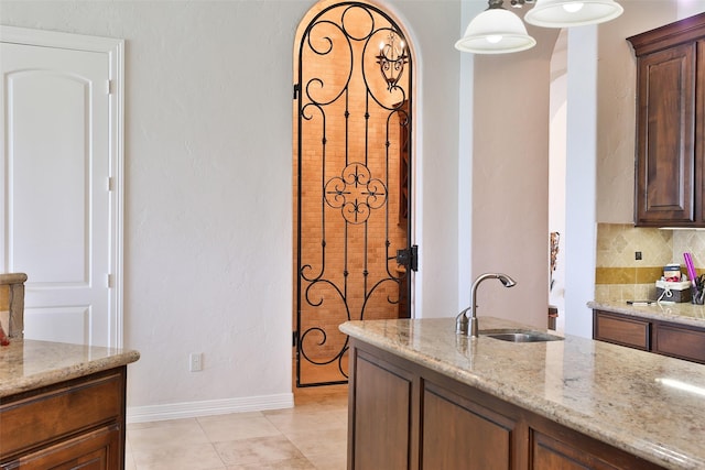 kitchen with light stone countertops, sink, hanging light fixtures, decorative backsplash, and light tile patterned floors