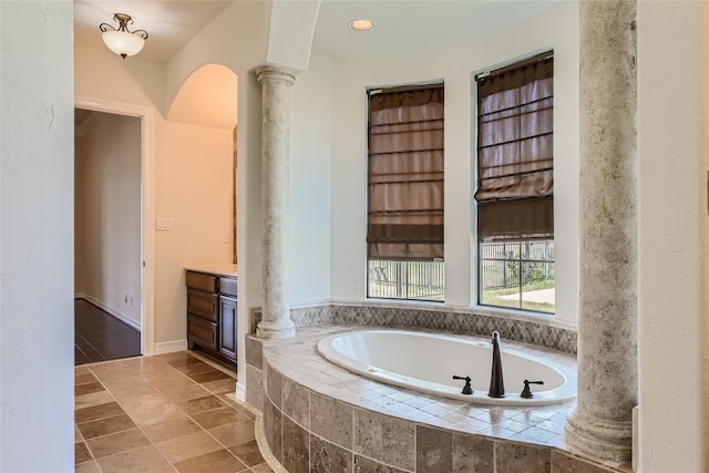 bathroom with ornate columns, vanity, and a relaxing tiled tub