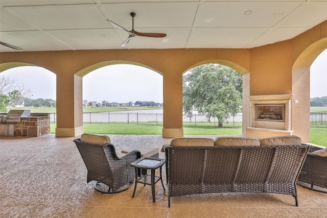 view of patio with an outdoor kitchen, a water view, ceiling fan, and an outdoor fireplace