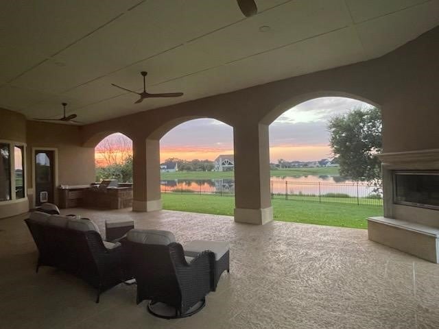 patio terrace at dusk with a lawn, ceiling fan, a water view, and exterior kitchen