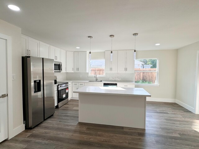 kitchen featuring appliances with stainless steel finishes, sink, a kitchen island, white cabinetry, and decorative light fixtures