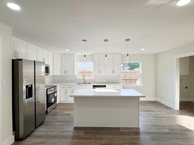 kitchen with appliances with stainless steel finishes, sink, a kitchen island, white cabinetry, and pendant lighting