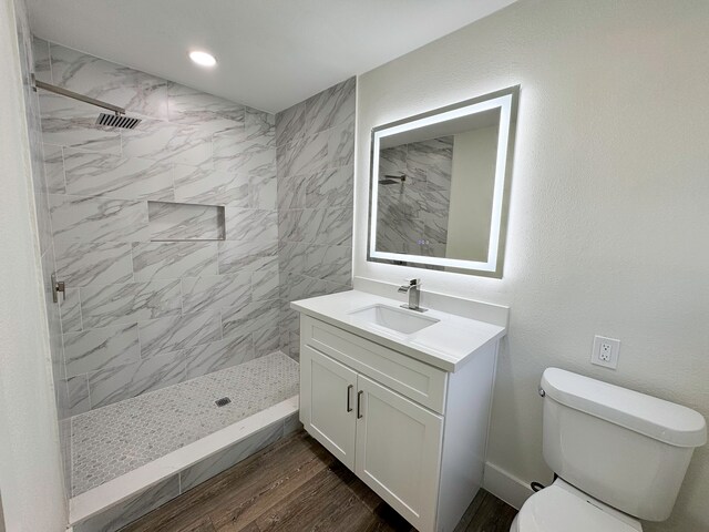 bathroom featuring vanity, toilet, wood-type flooring, and tiled shower