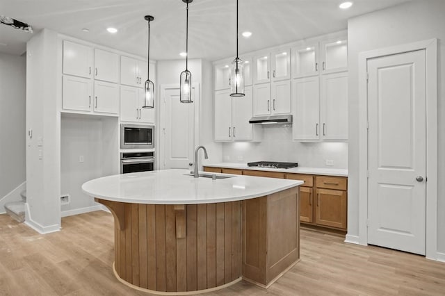 kitchen with a center island with sink, stainless steel appliances, hanging light fixtures, sink, and white cabinetry