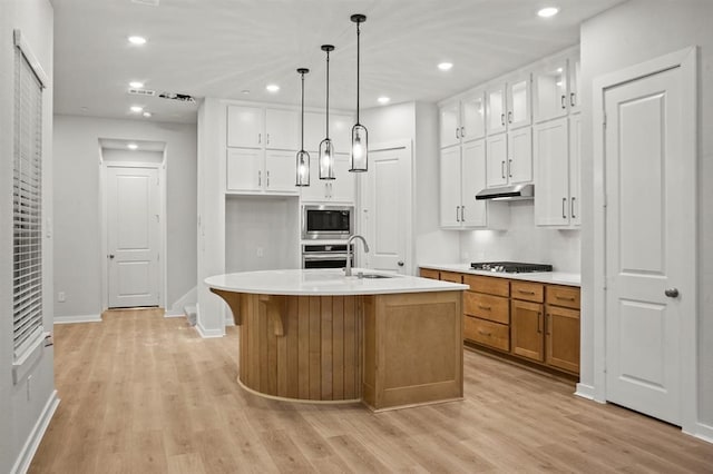 kitchen featuring stainless steel appliances, sink, decorative light fixtures, white cabinetry, and a kitchen island with sink