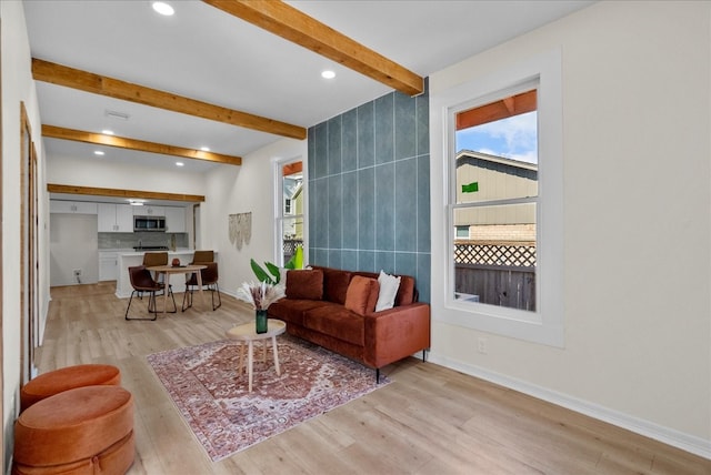 living room featuring beam ceiling, light hardwood / wood-style floors, and a healthy amount of sunlight