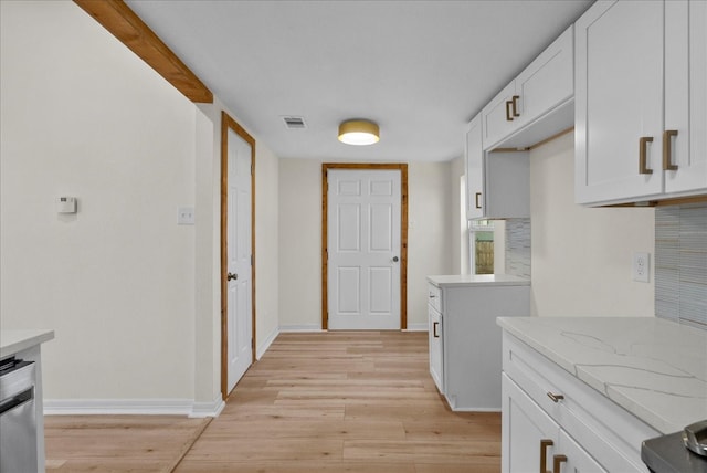 kitchen with white cabinetry, light stone countertops, light wood-type flooring, and decorative backsplash