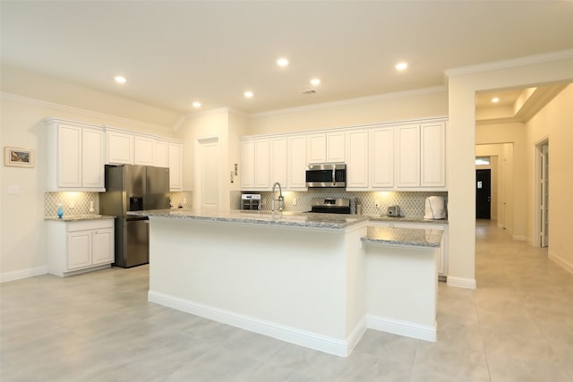 kitchen with white cabinets, a center island with sink, light stone counters, backsplash, and stainless steel appliances